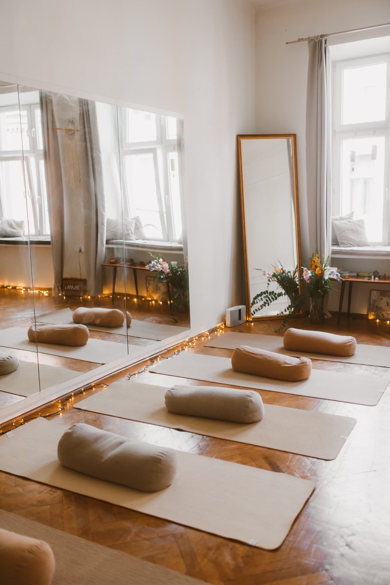 The room in window light: mats, linen bolsters, a gold-framed mirror and fairy lights