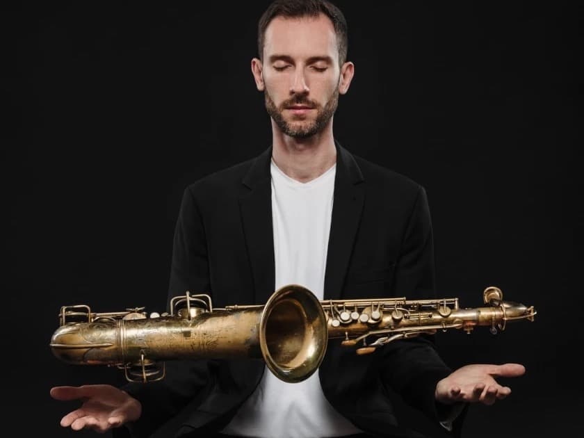 Sławomir Pezda with a saxophone, sitting in a meditative pose