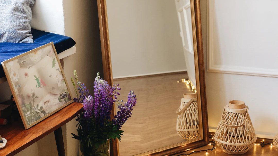 A gold mirror, lupins in a vase, a lantern and fairy lights on the parquet