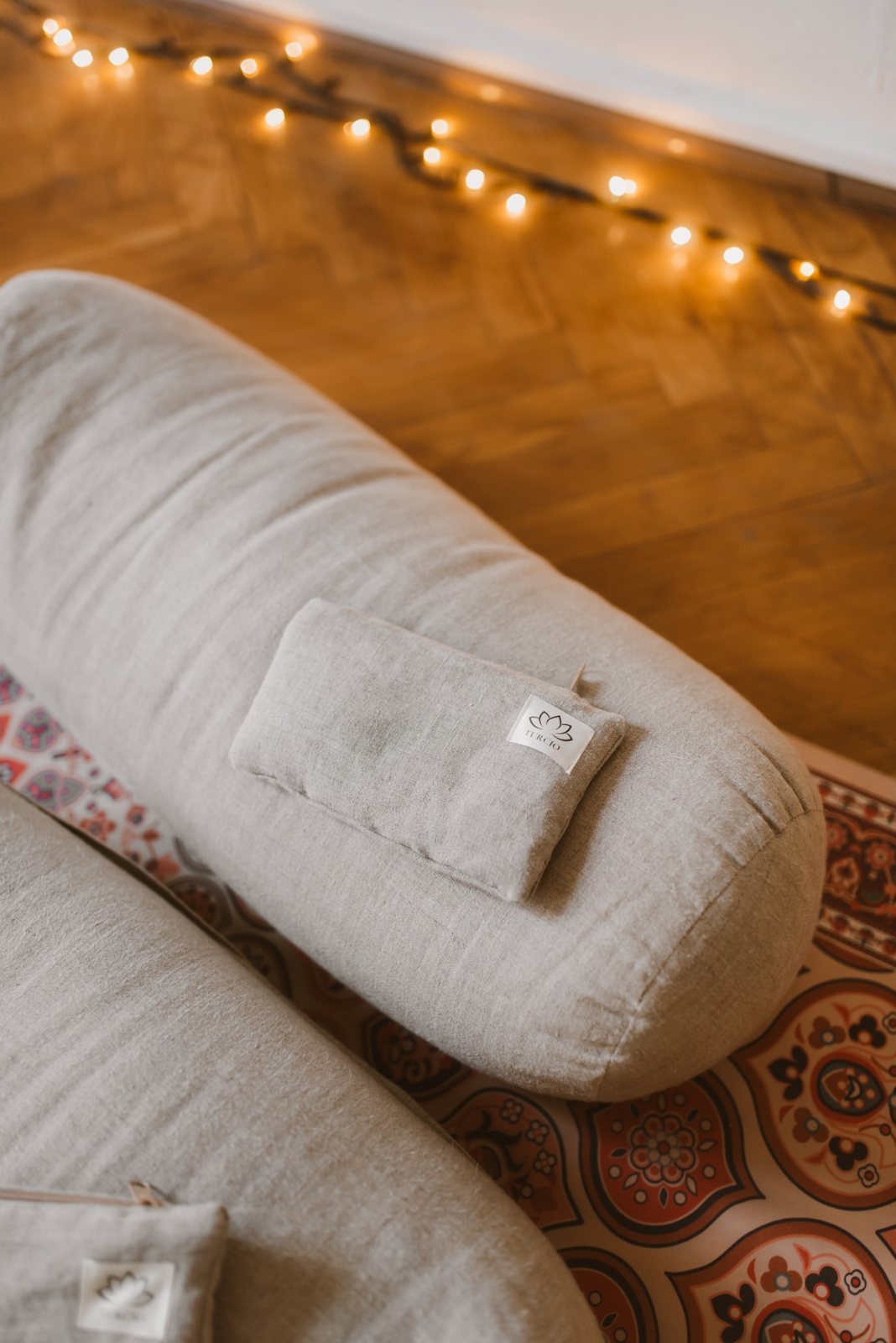 A linen bolster with a turcio tag in the glow of fairy lights