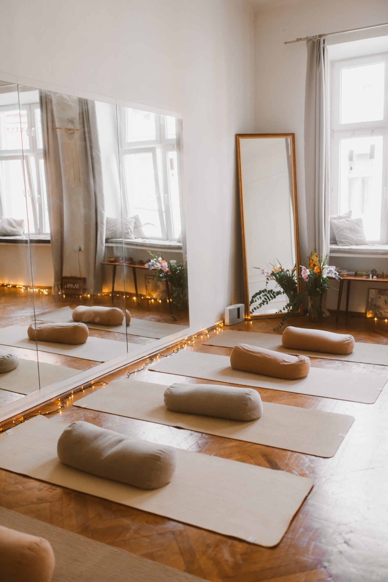 The room in window light: mats, linen bolsters, a gold-framed mirror and fairy lights